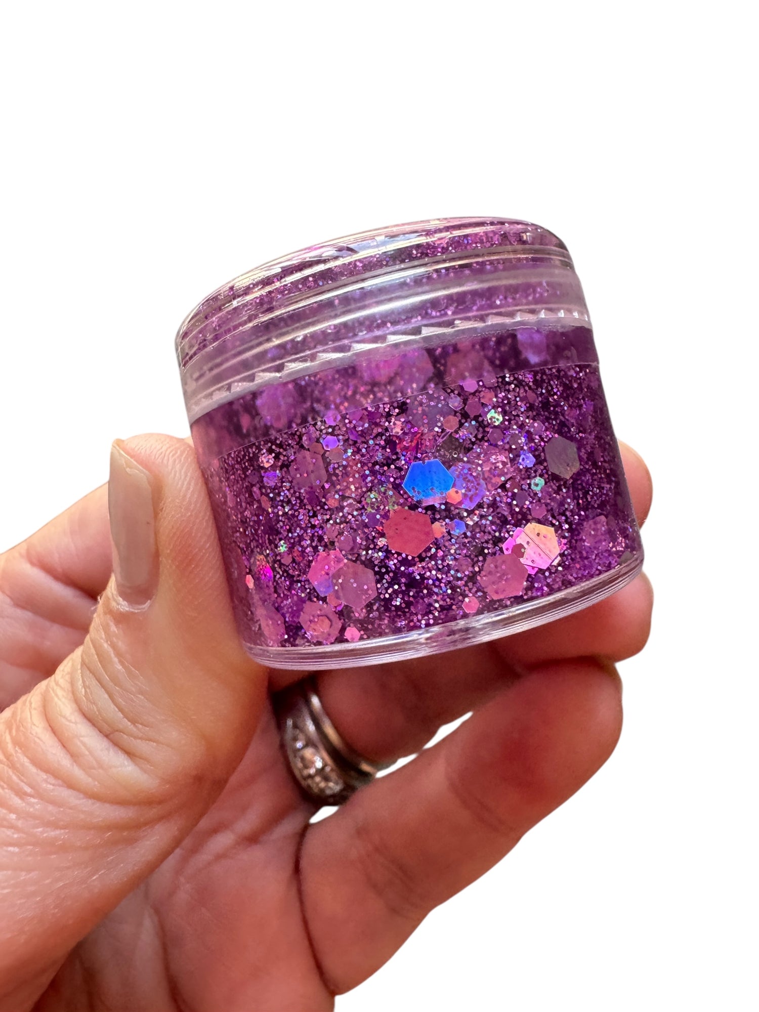Hand holding a small jar of purple glitter against a white background