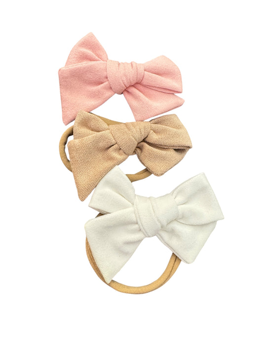 Three fabric hair bows in pink, beige, and white on a white background