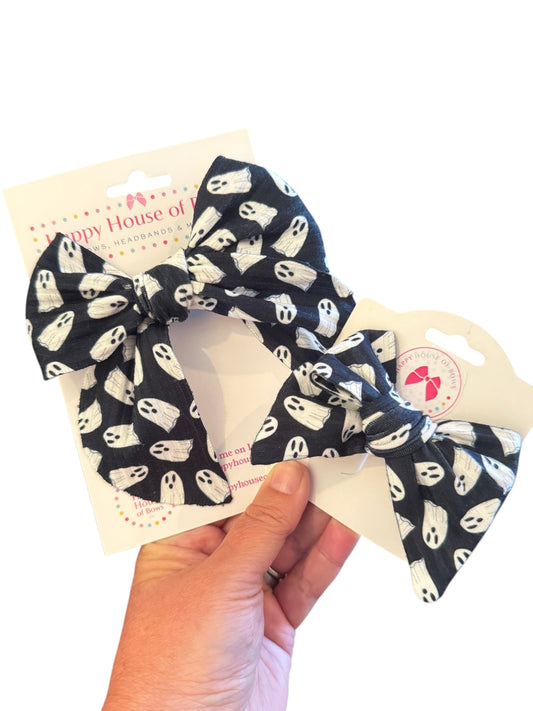 Black hair bow with white ghost pattern held by a hand on a white background