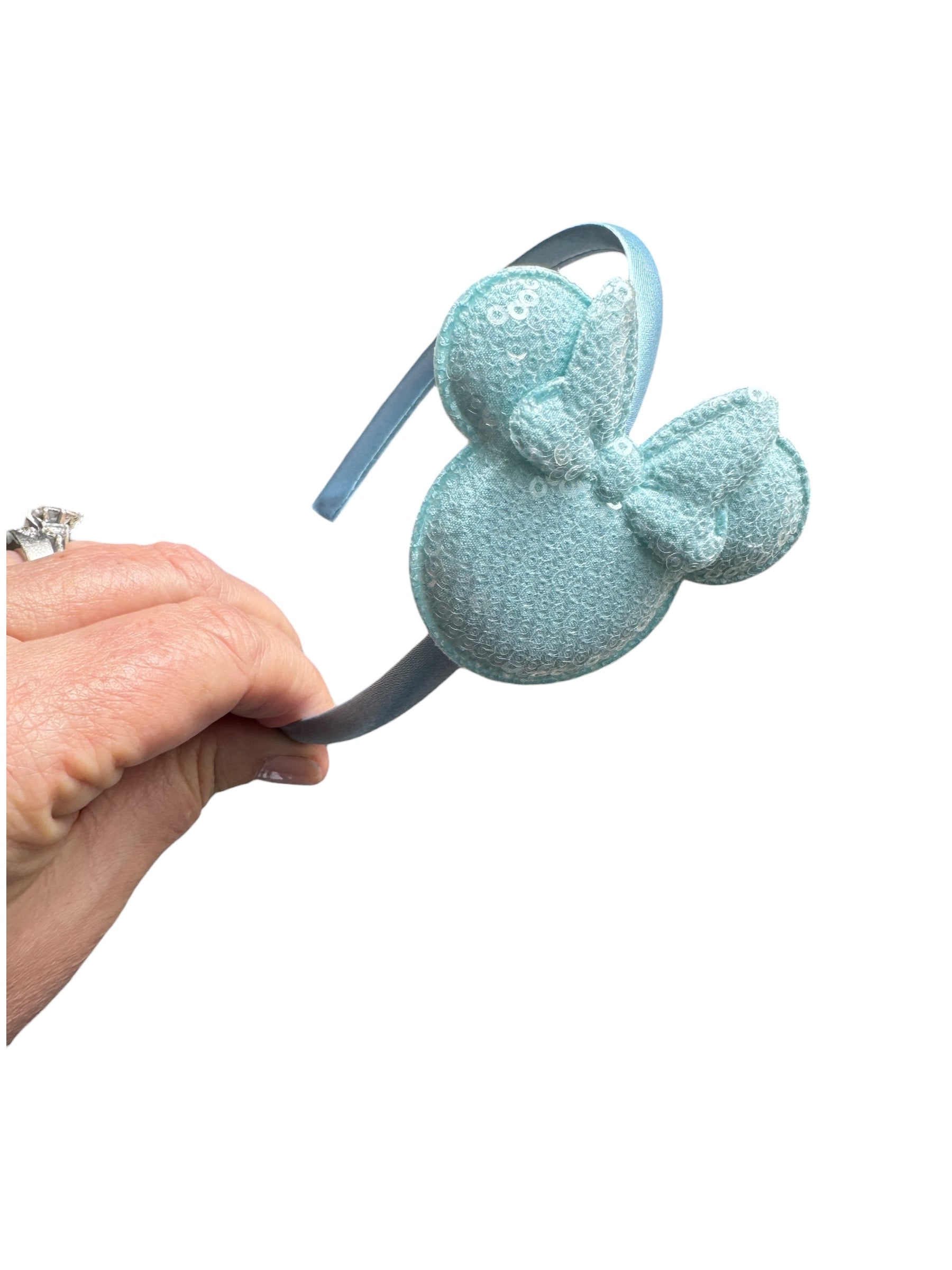 Light blue mouse ear headband with bow held by a hand on a white background