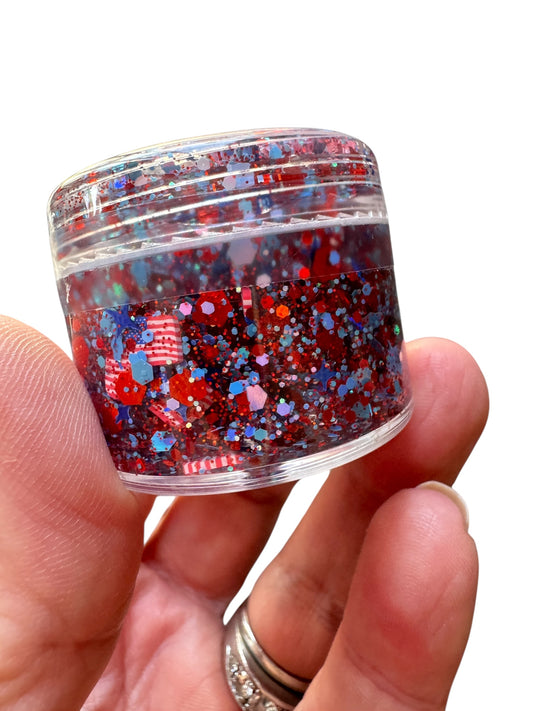Hand holding a small container of multicolored glitter hair gel against a white background