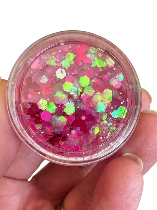 Hand holding a small container of pink glitter hair and body gel with a white background