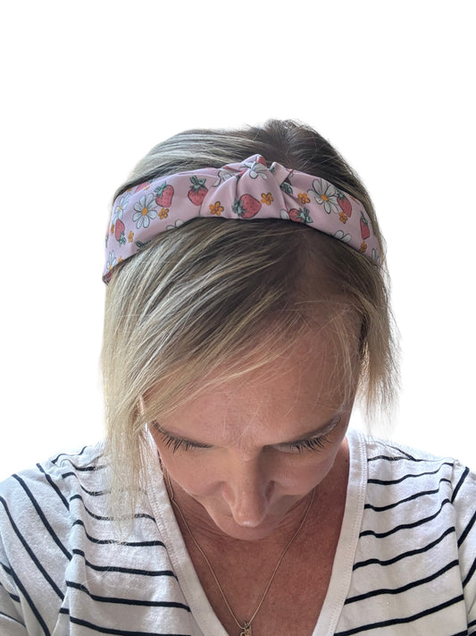A pink headband with a floral pattern including strawberries and daisies.