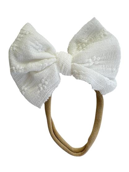White textured bow on a beige headband against a white background