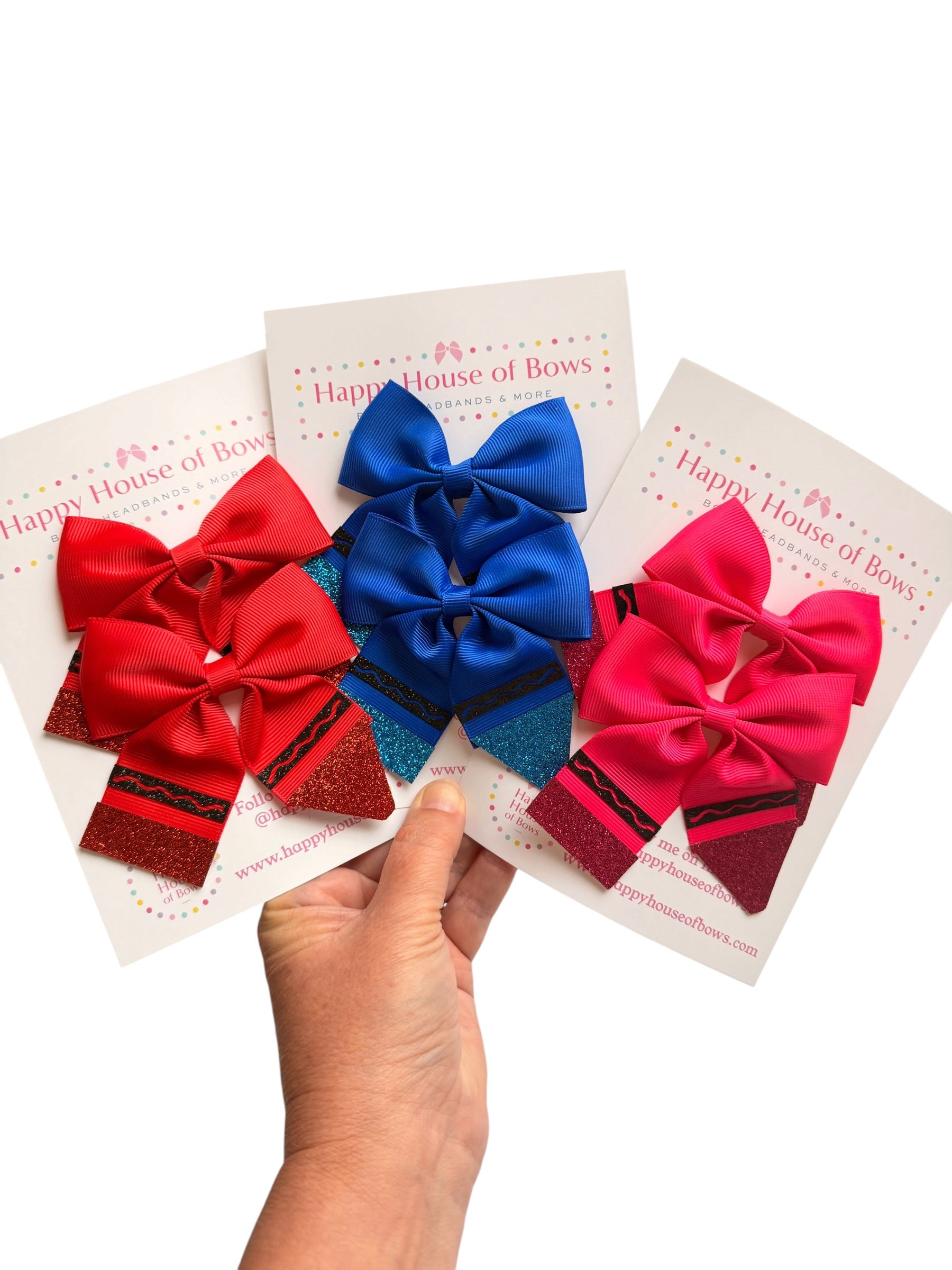 Three decorative hair bows in red, blue, and pink are displayed on white backing cards held by a hand against a white background. The cards are branded Happy House of Bow.