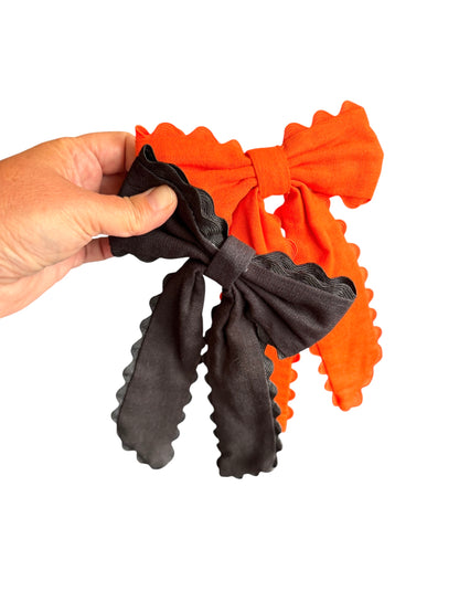 Hand holding two fabric bows, one orange and one black, on a white background.