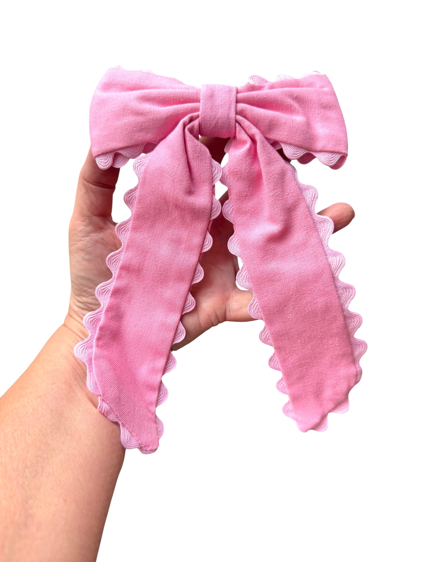 Pink hair bow with ruffled edges held by a hand on a white background