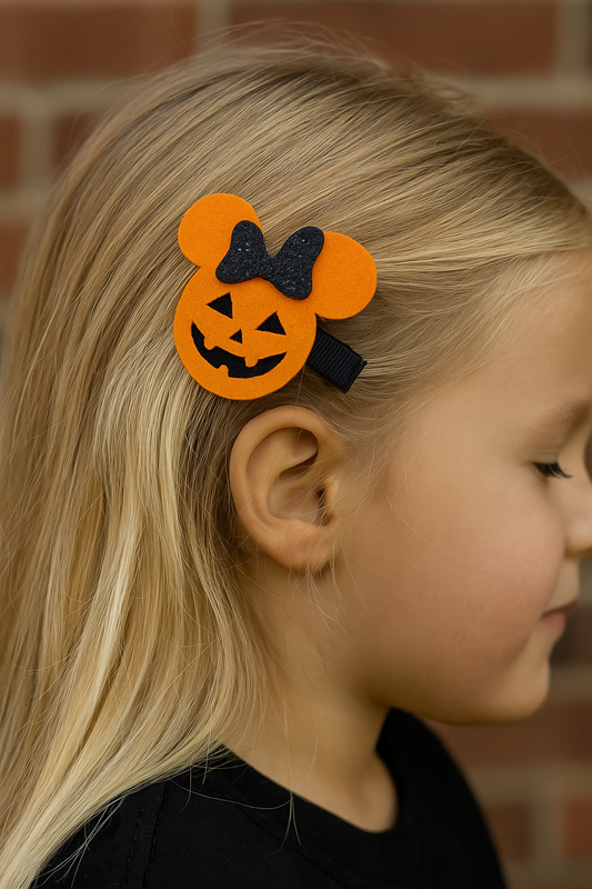 Child with a Halloween-themed hair clip featuring an orange pumpkin design and black bow.