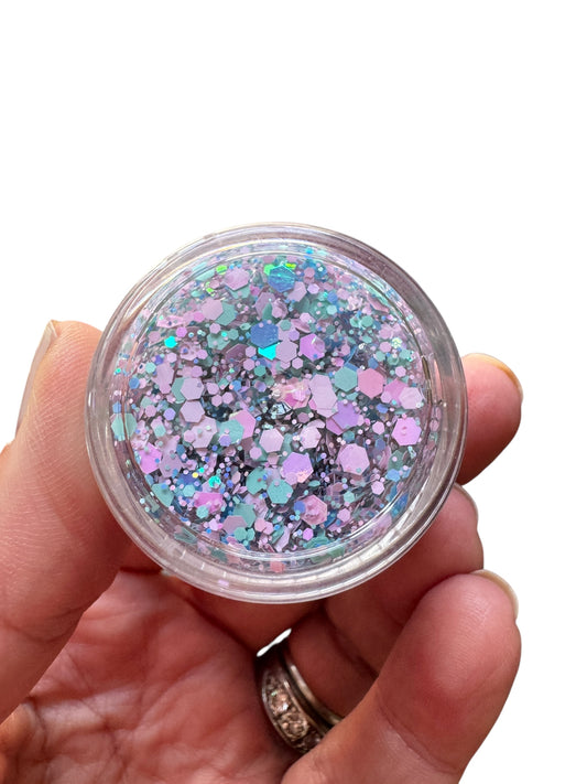 Hand holding a small container of multicolored glitter hair gel against a white background