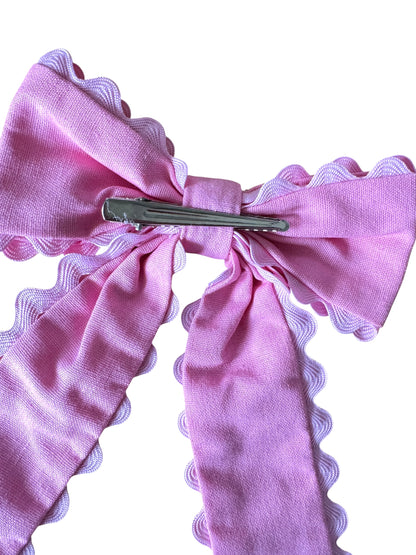 Pink bow hair clip with scalloped edges on a white background