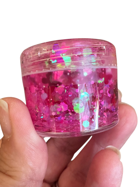 Hand holding a small container of pink glitter hair and body gel with a white background