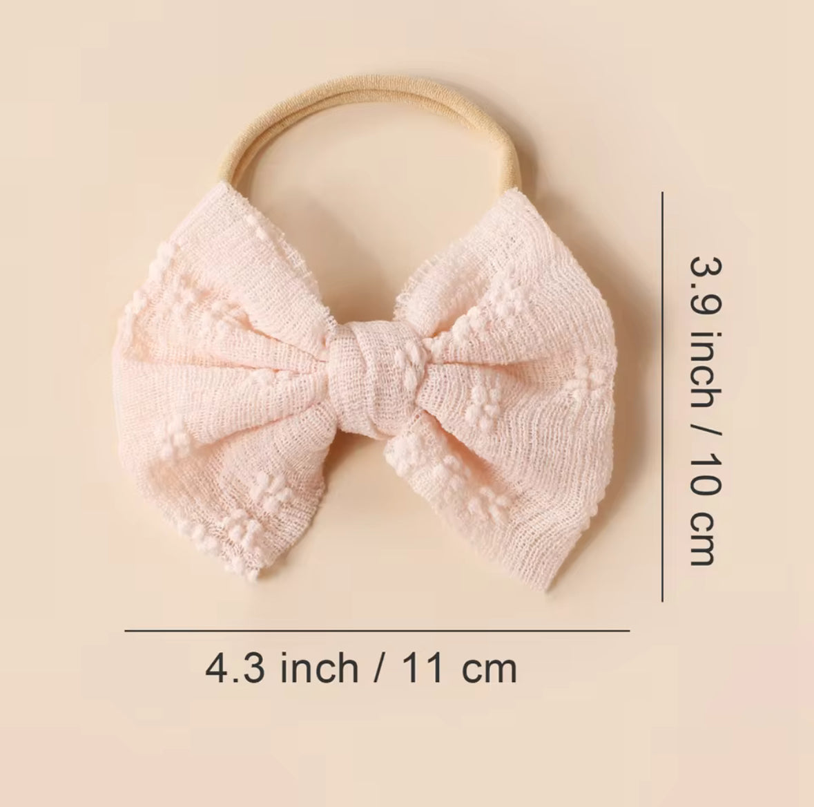 Pink knitted bow headband with measurements on a beige background