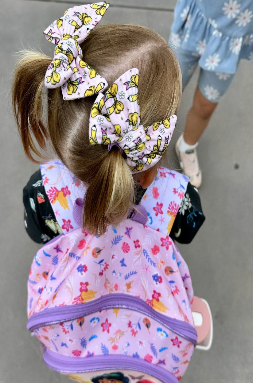 Child with a colorful backpack and hair bows on a neutral background