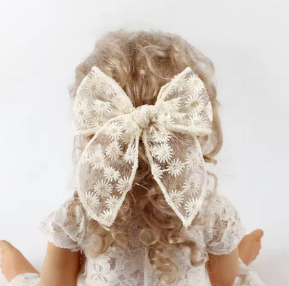 little girl wearing a large lace bow in their hair against a white background