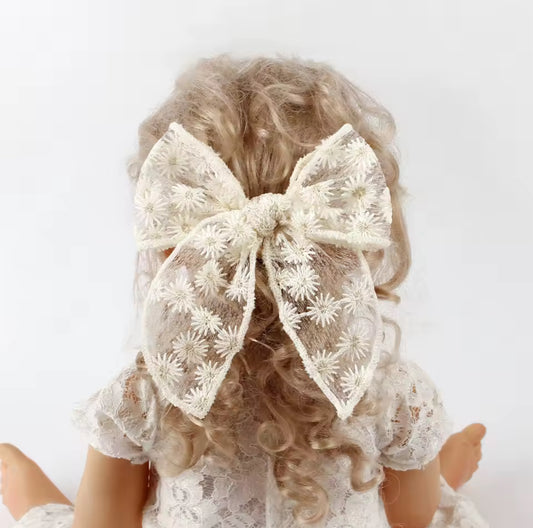 little girl wearing a large lace bow in their hair against a white background