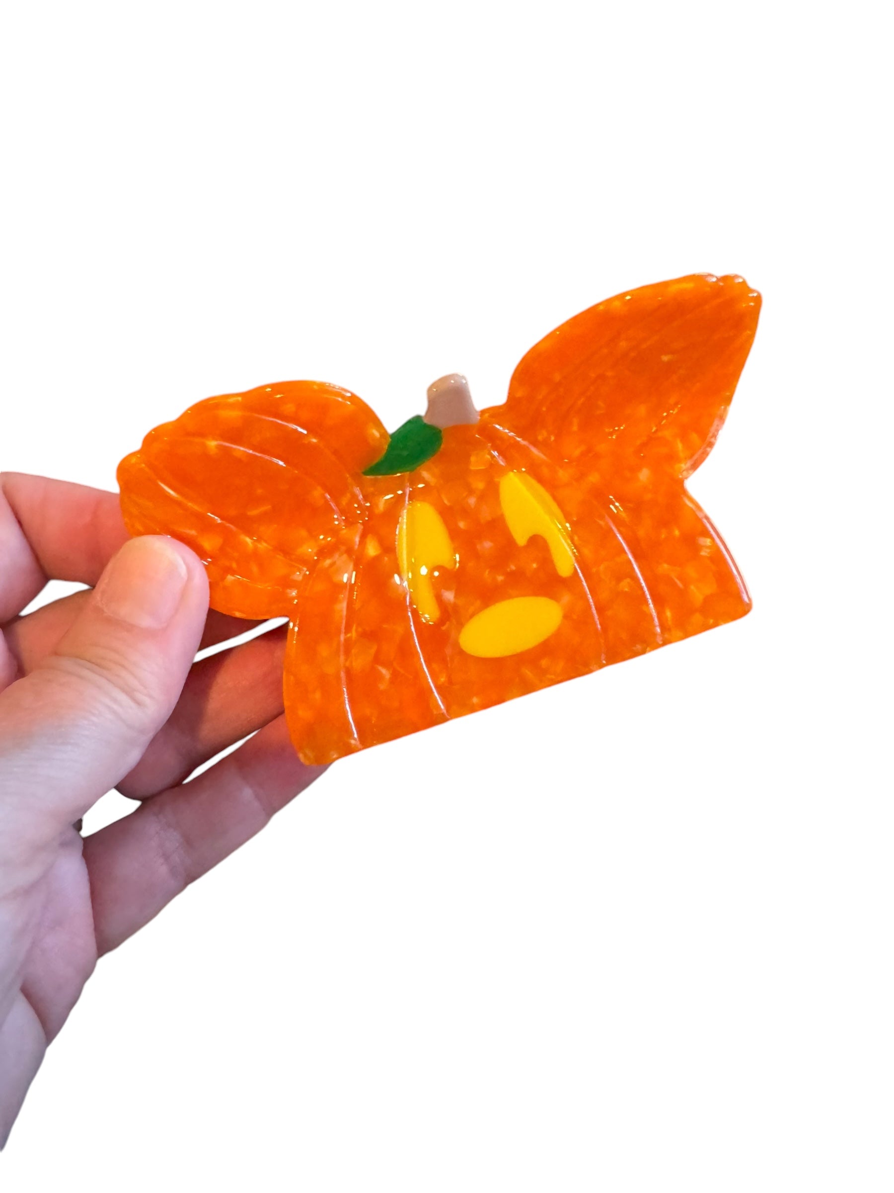 An orange pumpkin-shaped Halloween mouse ear claw clip held in a hand against a white background