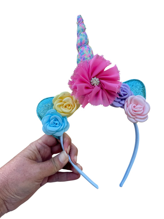Colorful unicorn horn headband with flowers held by a hand on a white background