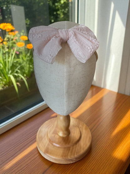 Mannequin head with a white lace headband on a wooden stand in front of a window with flowers outside.