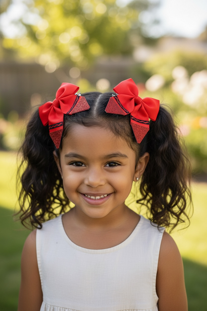 A young girl with curly dark hair wearing two large red bow hair clips, photographed outdoors in a sunny garden setting.