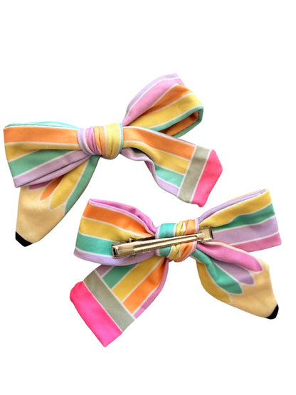 Two pastel rainbow striped hair bows with a gold metal barrette clasp, displayed on a solid white background.