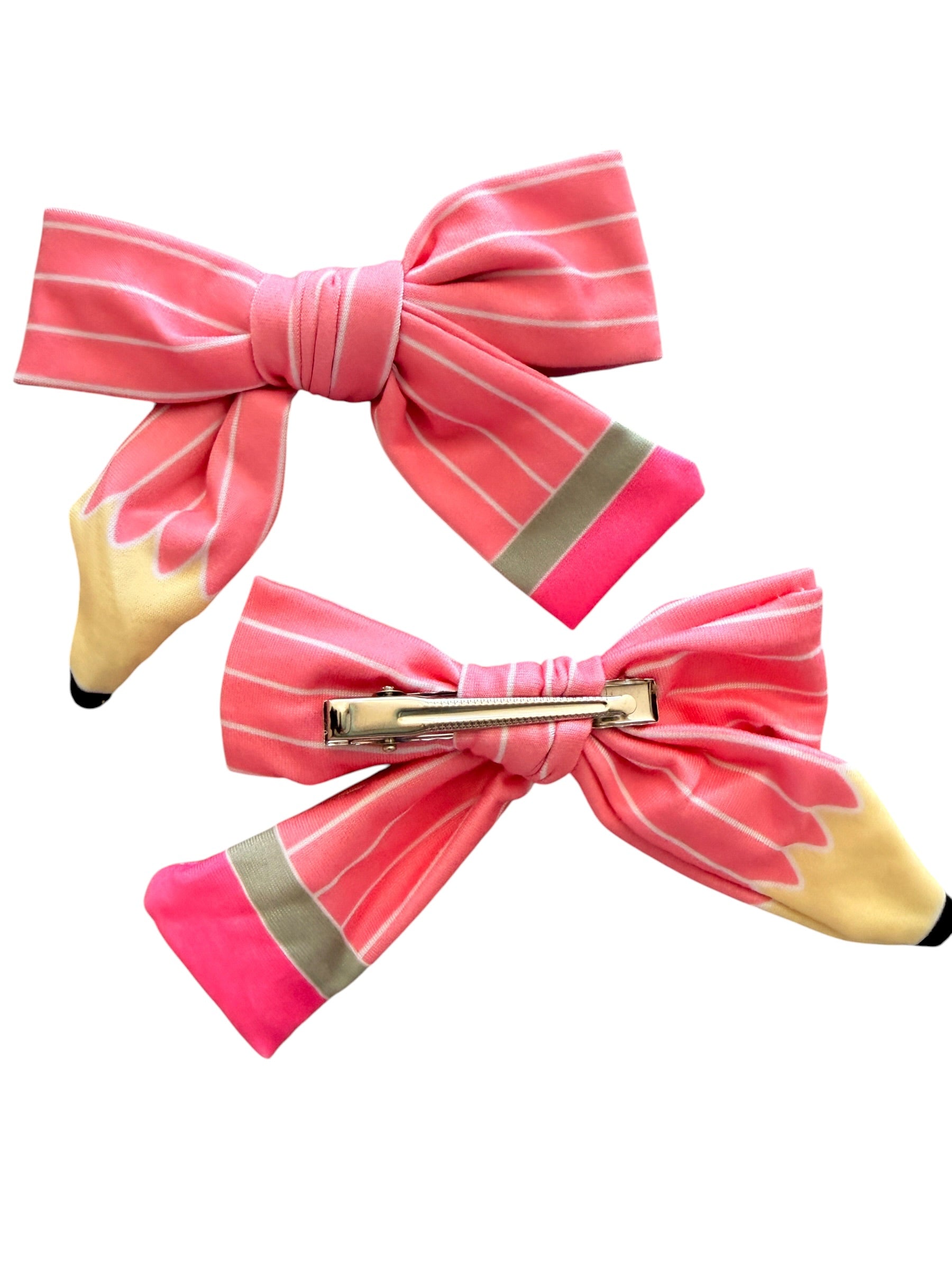 Two pink striped bow hair clips designed to look like pencil tips, shown on a plain white background. One clip is shown from the front and the other from the back to display the metal pin fastener.