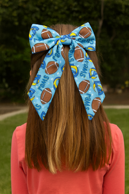 Person wearing a large blue hair bow with football and sports designs outdoors.