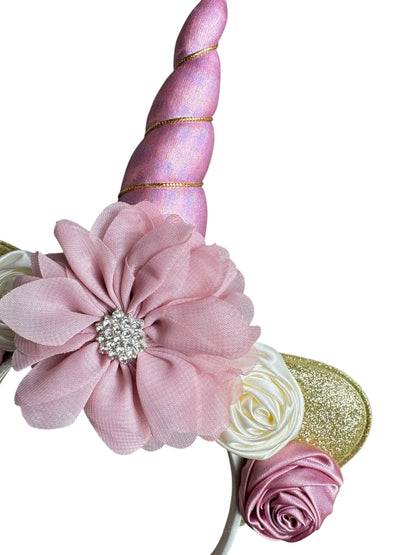 Decorative hair bow with pink flower, unicorn horn, and gold accents on a white background