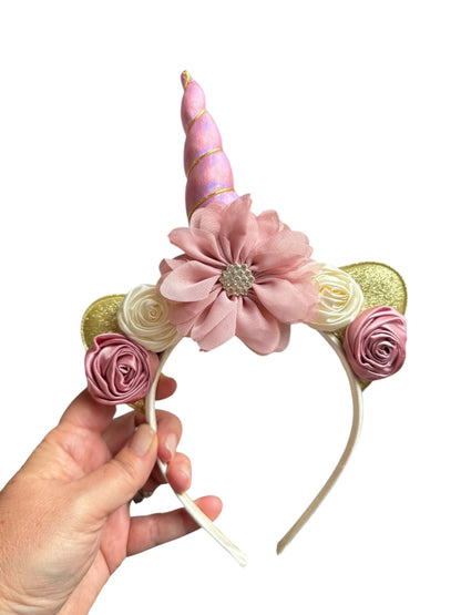 Unicorn horn headband with flowers held by a hand on a white background