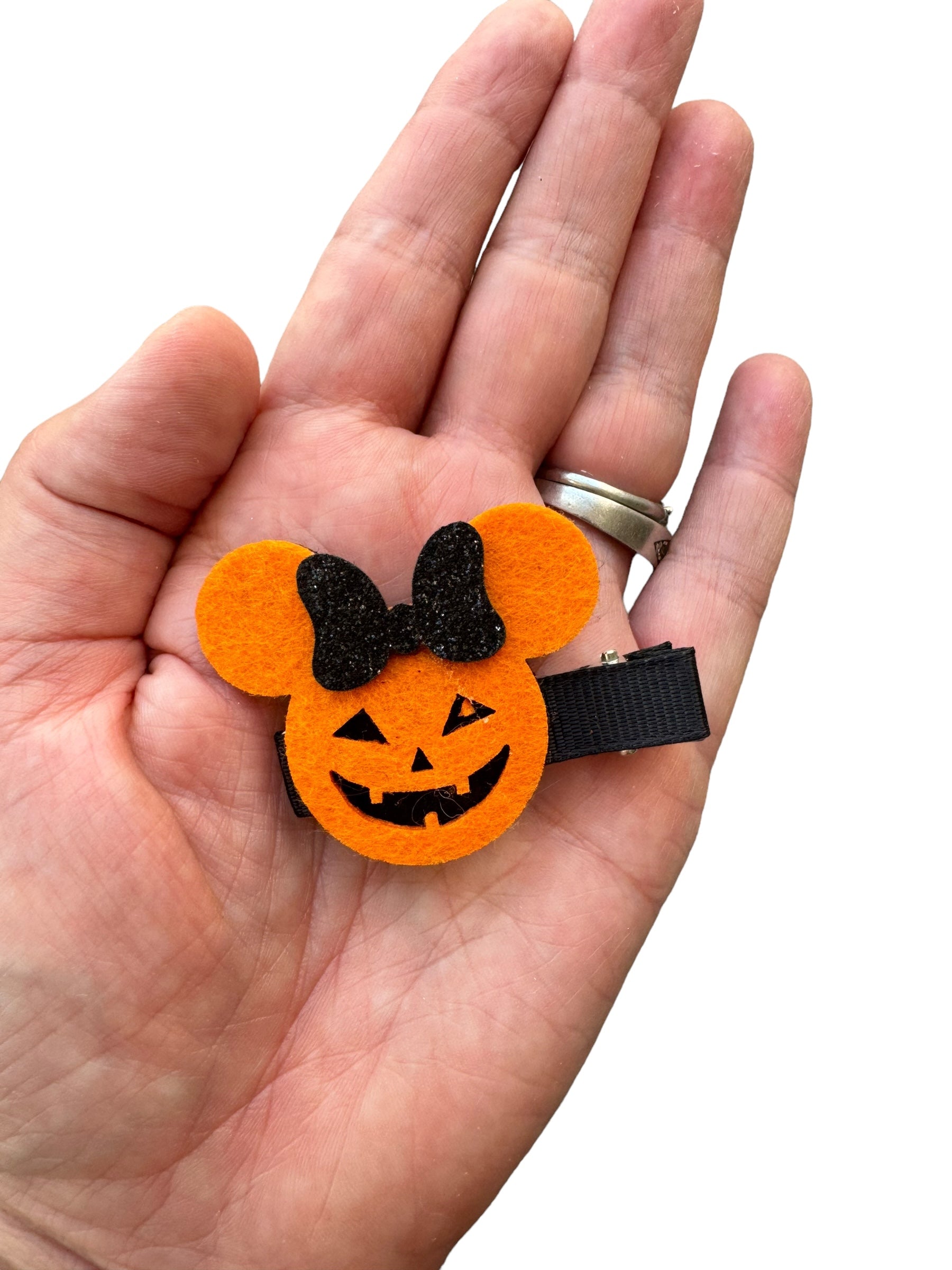 Halloween pumpkin mouse hair clip with a black glitter bow in a persons hand