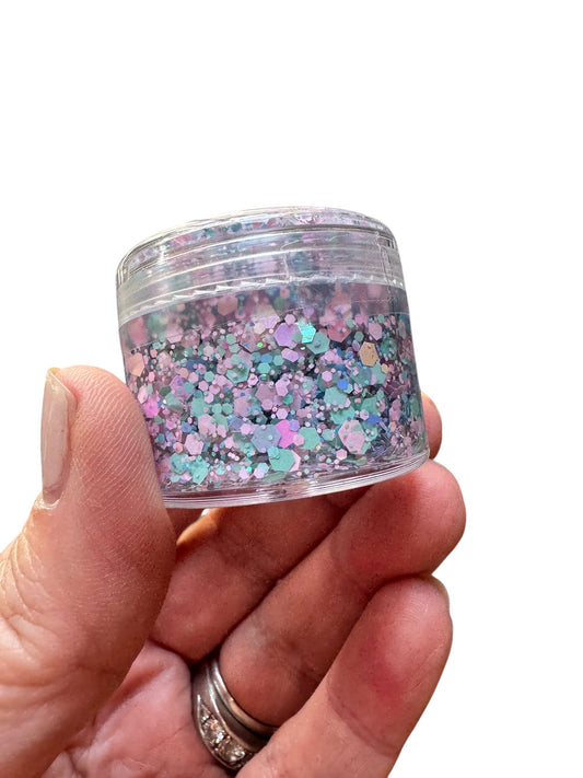 Clear container filled with multicolored glitter hair gel held by a hand on a white background