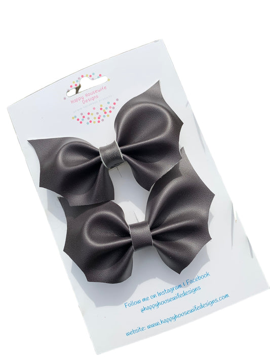 A set of faux leather hair bows in various colors with an alligator clip attached, displayed on a card.