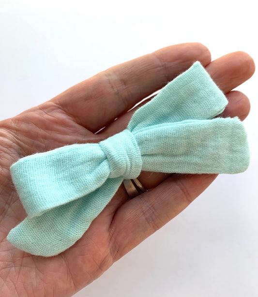 A hand holding a mint mini Muslin hair bow clip.